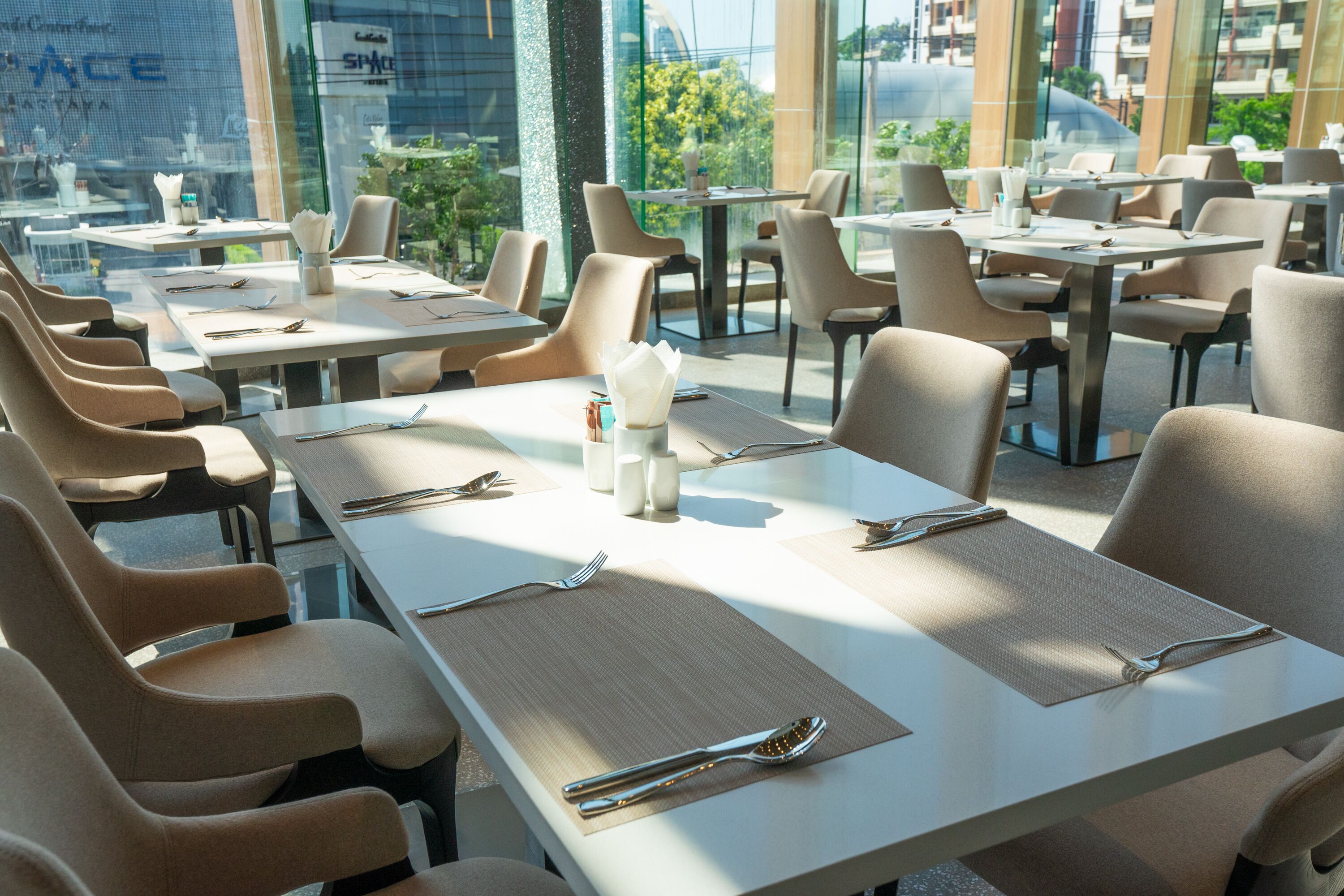 Un restaurante moderno con mesas y sillas ordenadas, vistas amplias al exterior gracias a grandes ventanales y una decoración interior limpia y minimalista.