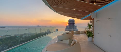 A rooftop pool with a view of the sunset and a cityscape.