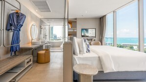 A modern hotel room with a large bed, a sitting area, a vanity with a mirror, and a view of the city and sea. - Akara Hotel Pattaya (Pattaya)