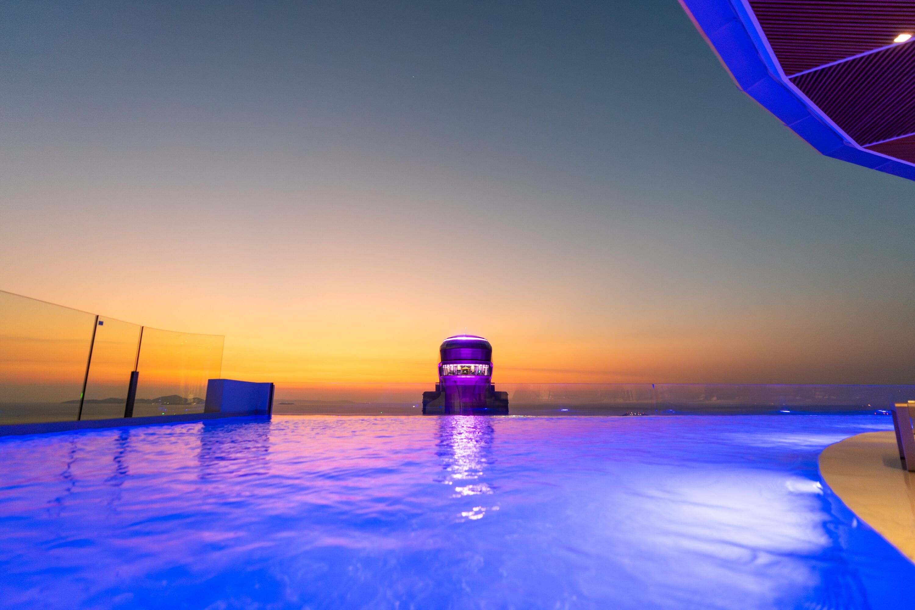 Ein Infinity-Pool mit Blick auf den Sonnenuntergang und einer markanten, architektonischen Struktur in der Mitte.