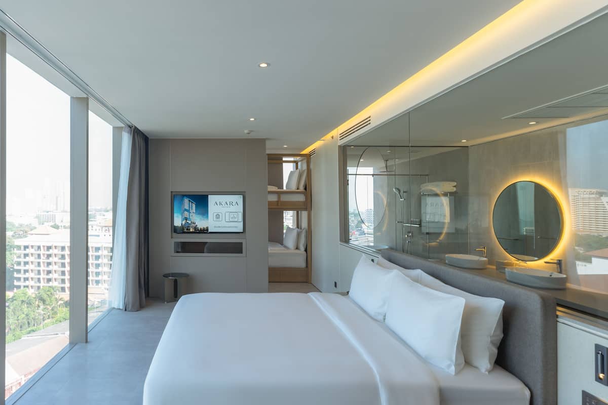 A modern hotel room with a large bed, a TV mounted on the wall, a bathroom with a large mirror, and a view of the city through the window.