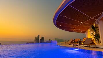 A modern hotel pool area with a city skyline view at sunset.