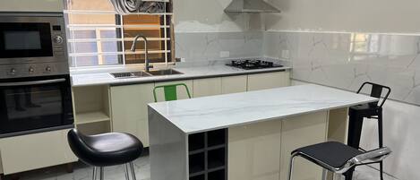A compact kitchen with a built-in oven, a gas stove, a sink, and a small dining area with two stools.