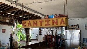 A rustic kitchen with a wooden bar counter, a stainless steel refrigerator, and a hanging sign that reads "CANTINA".