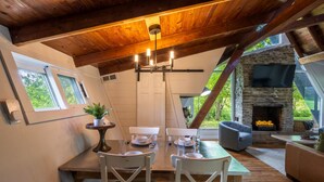A dining area with a wooden table, white chairs, a chandelier, and a stone fireplace. - Lakefront with Lake Access•Hot Tub•Firepit•Pets (Rockbridge)