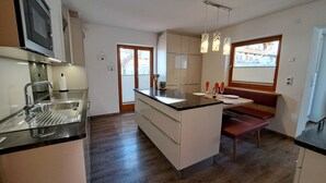 Une cuisine moderne dotée d’un îlot central, d’appareils électroménagers en acier inoxydable et de luminaires suspendus.
