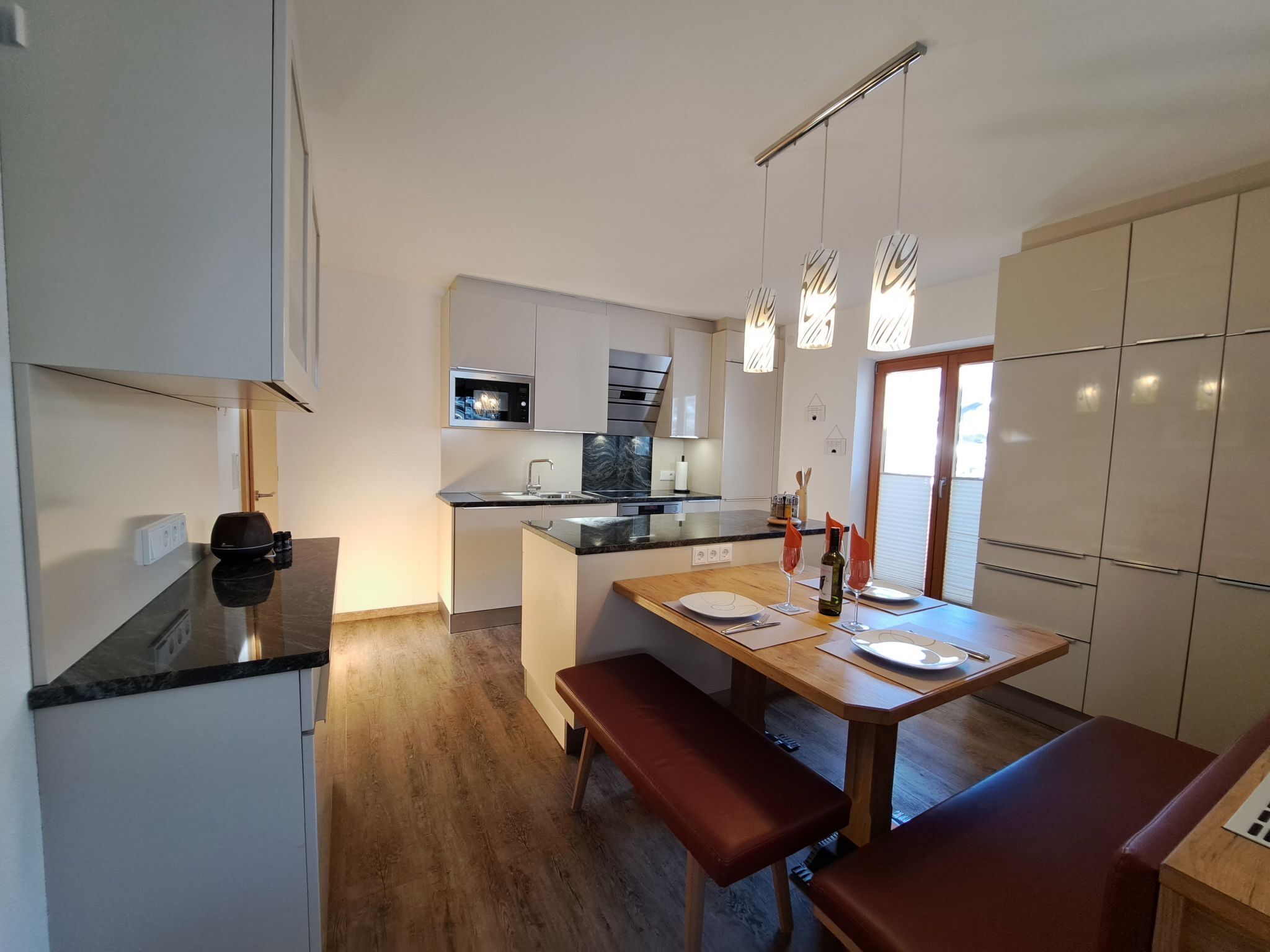 Una cocina moderna con microondas integrado, un fregadero y una zona de comedor con mesa de madera y bancos.