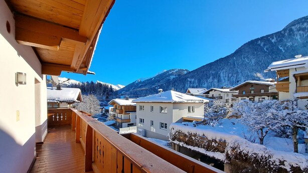 Un balcon en bois donnant sur un village enneigé, avec vue sur les montagnes.