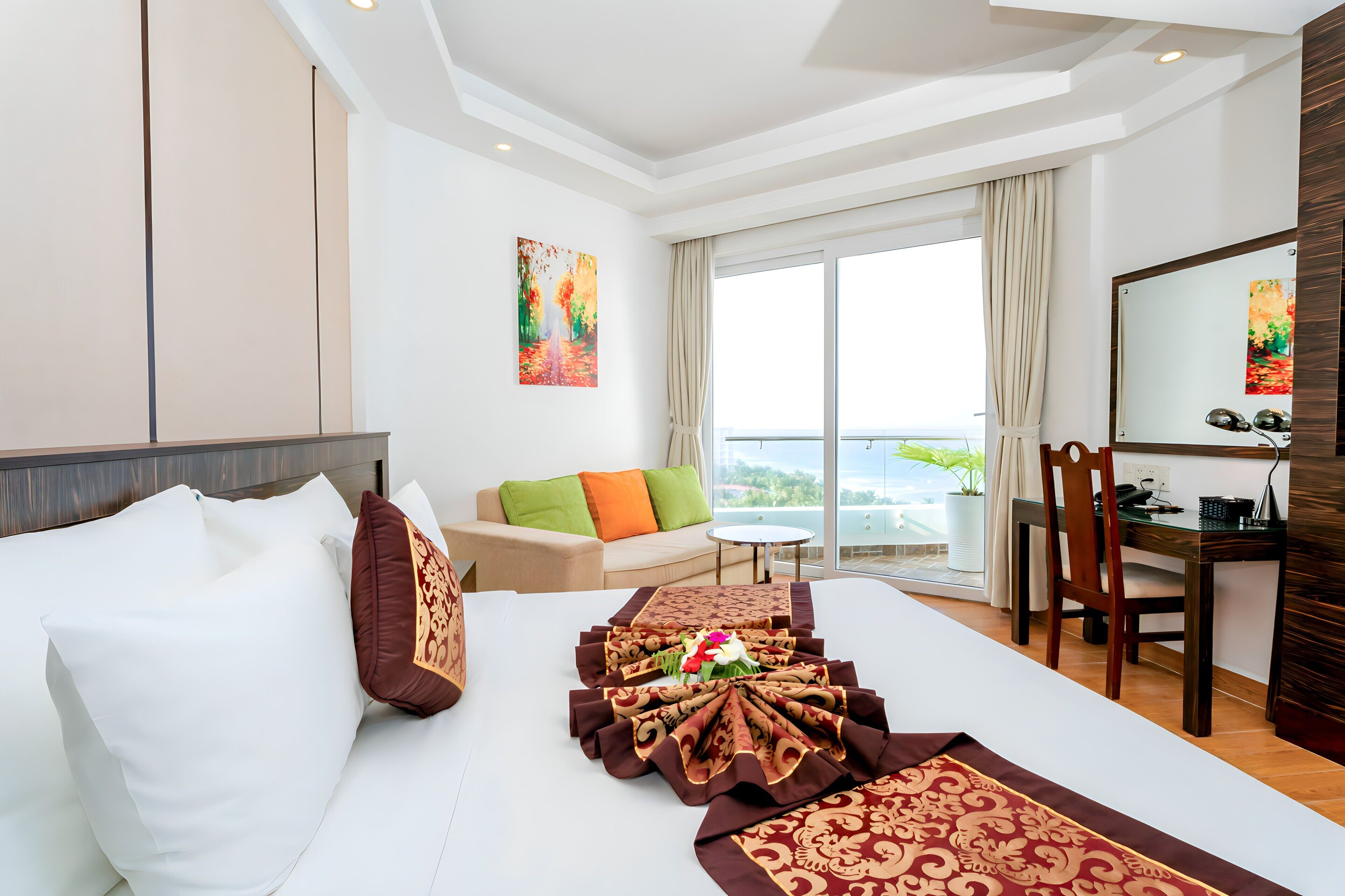 A hotel room with a bed, a sofa, a dining table, and a view of the outdoors.