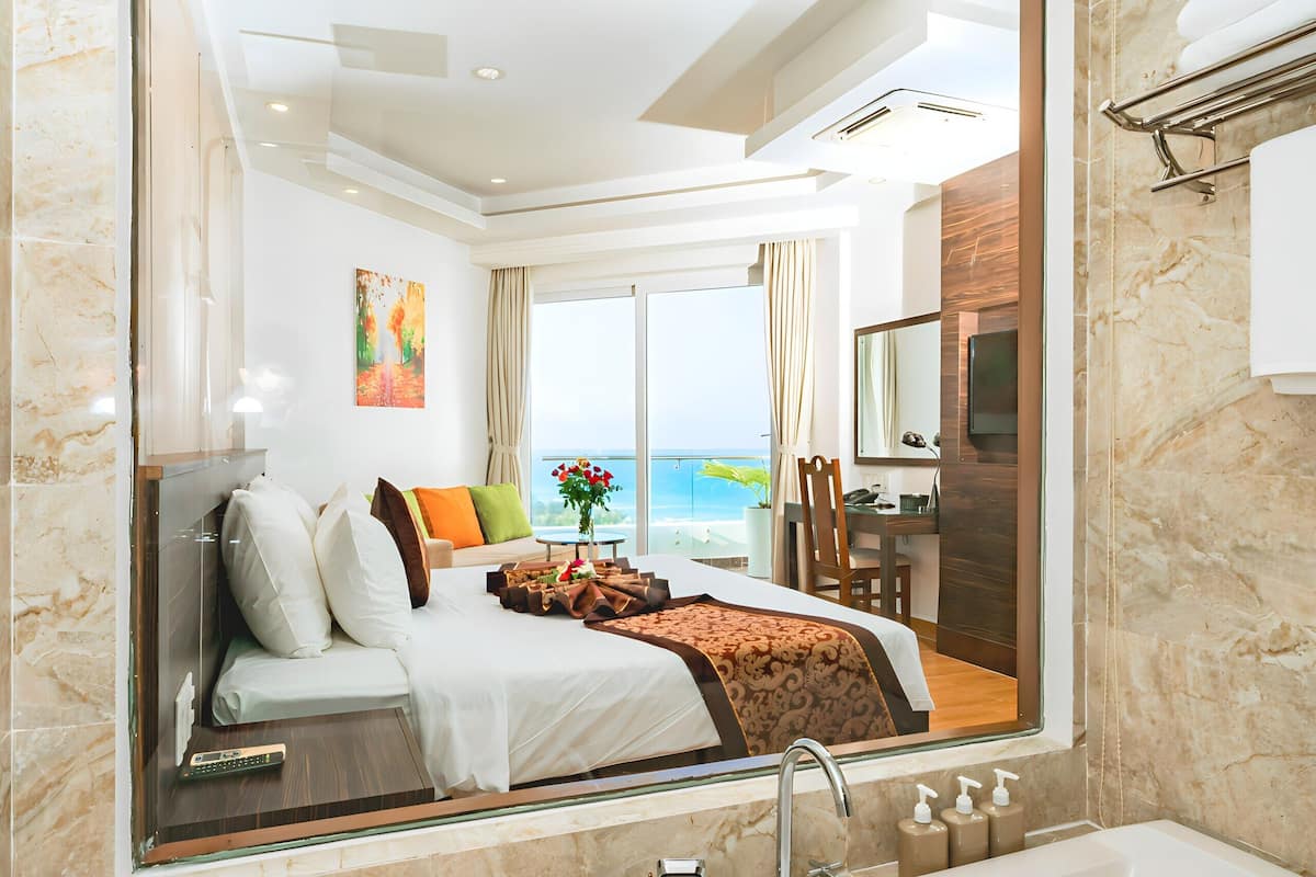 A modern hotel room with a large bed, a bathtub, and a view of the sea.