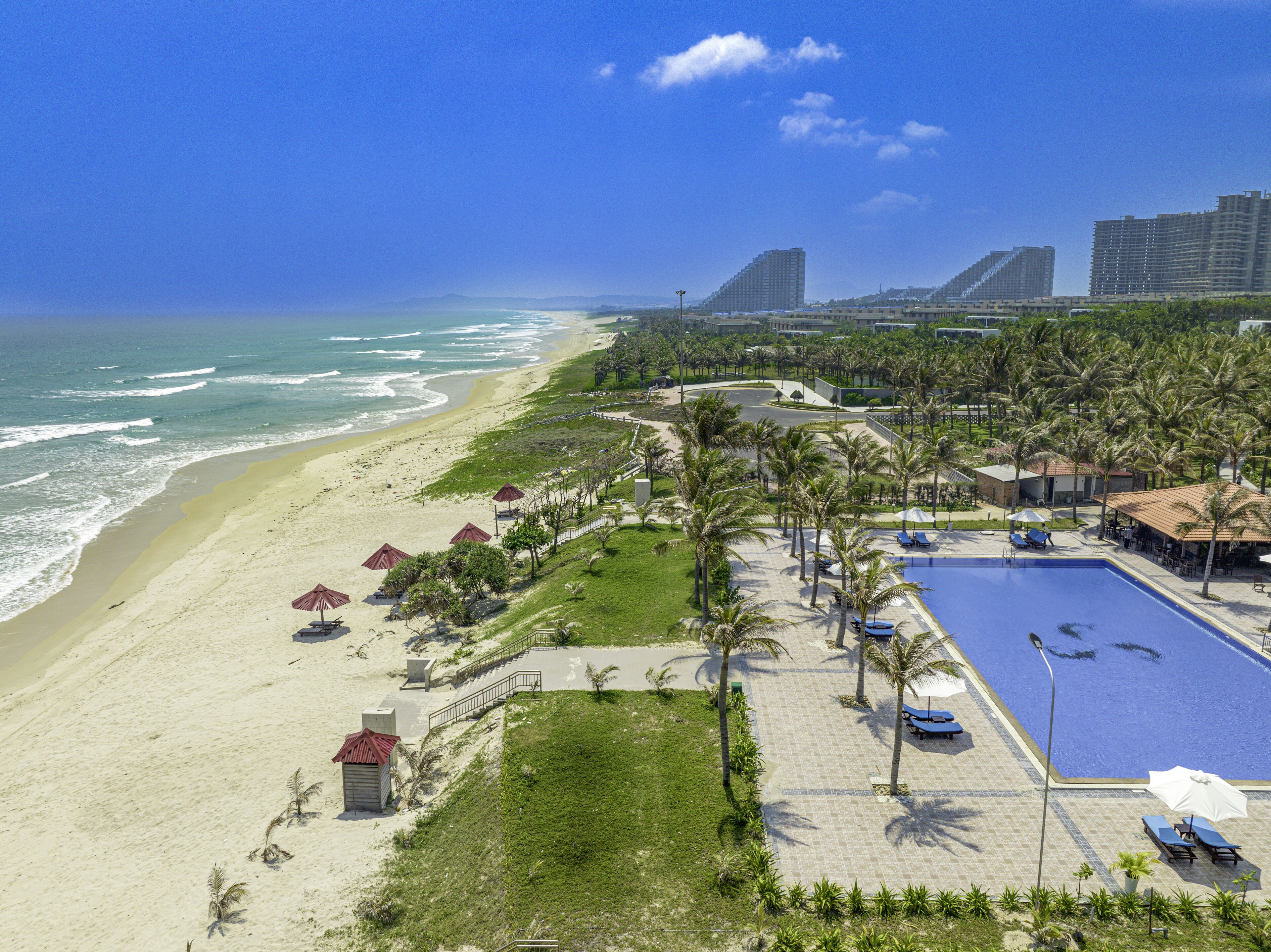 A beachfront resort with a swimming pool, palm trees, and a beach.