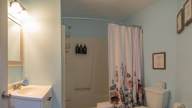 Une salle de bain avec une douche, des toilettes, un lavabo et une citation encadrée au mur.
