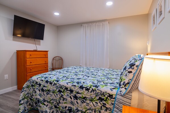 A bedroom with a bed, dresser, chair, and a TV mounted on the wall. - Charming Apt_Open Green Space on Front to Relax and Sunbath (Hancock)