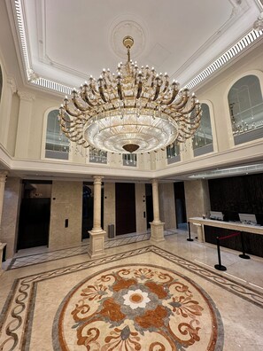 Un'imponente hall con un grande lampadario decorato, pavimento in marmo e architettura classica.