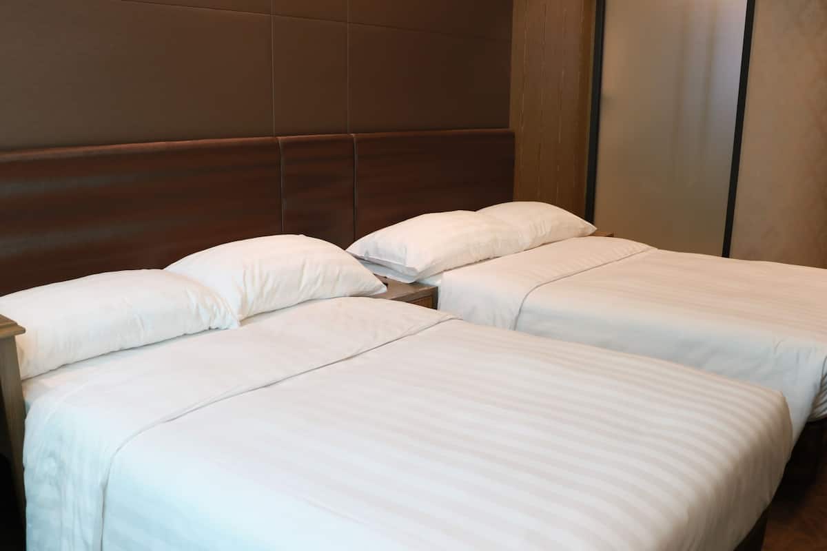 Ein Hotelzimmer mit zwei Betten, jeweils mit weißer Bettwäsche und einem hölzernen Kopfende.
