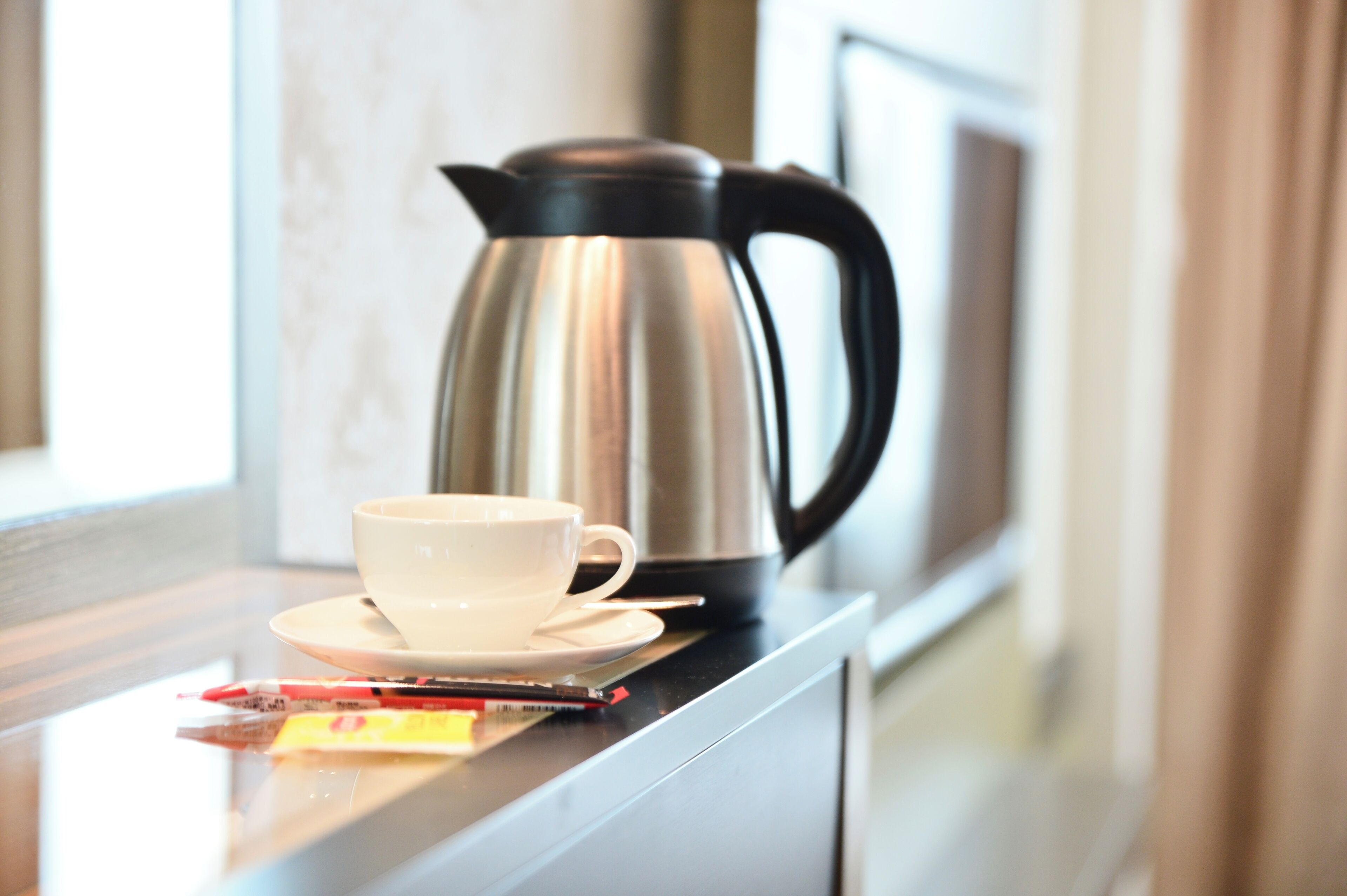 A stainless steel coffee pot and a white cup on a countertop.