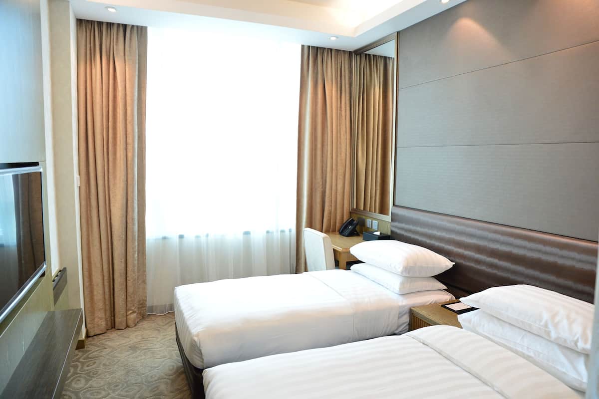 Ein Hotelzimmer mit zwei Betten, einem Schreibtisch, einem Stuhl, einem Fernseher und einem großen Fenster mit Vorhängen.