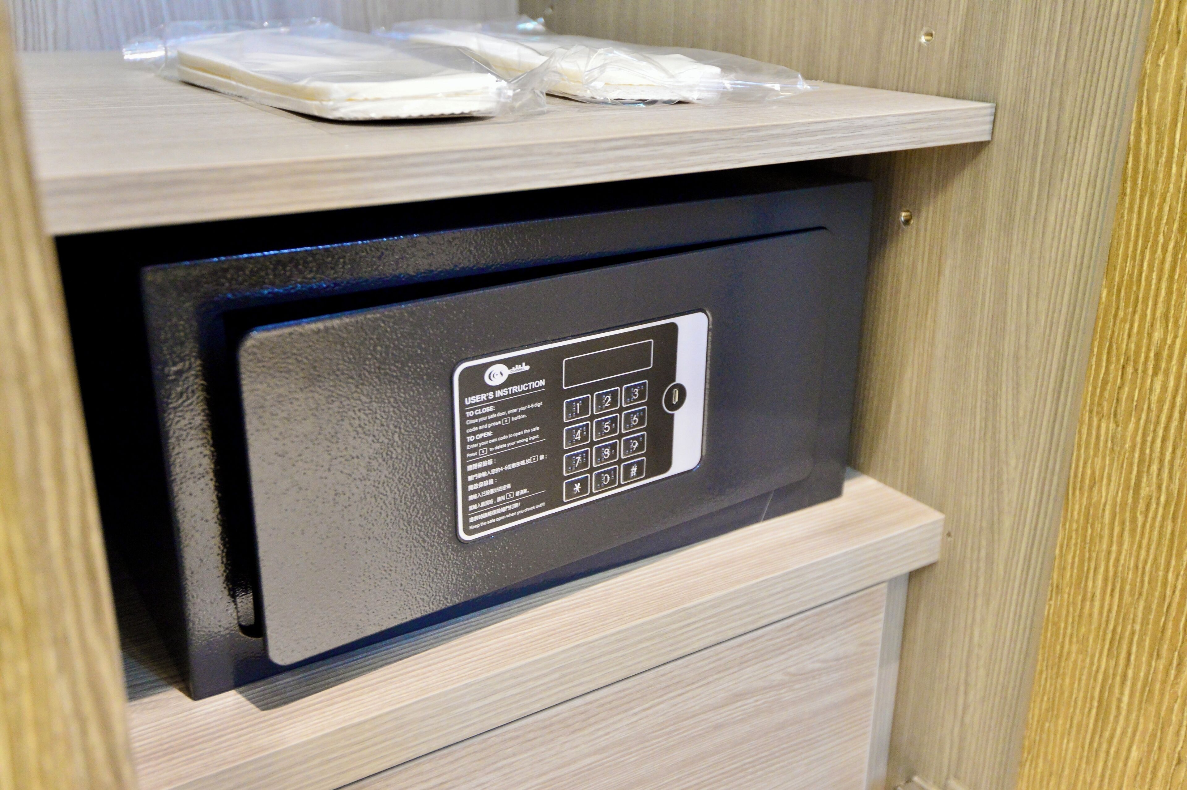 A black safe with a keypad and a user manual on a wooden counter.