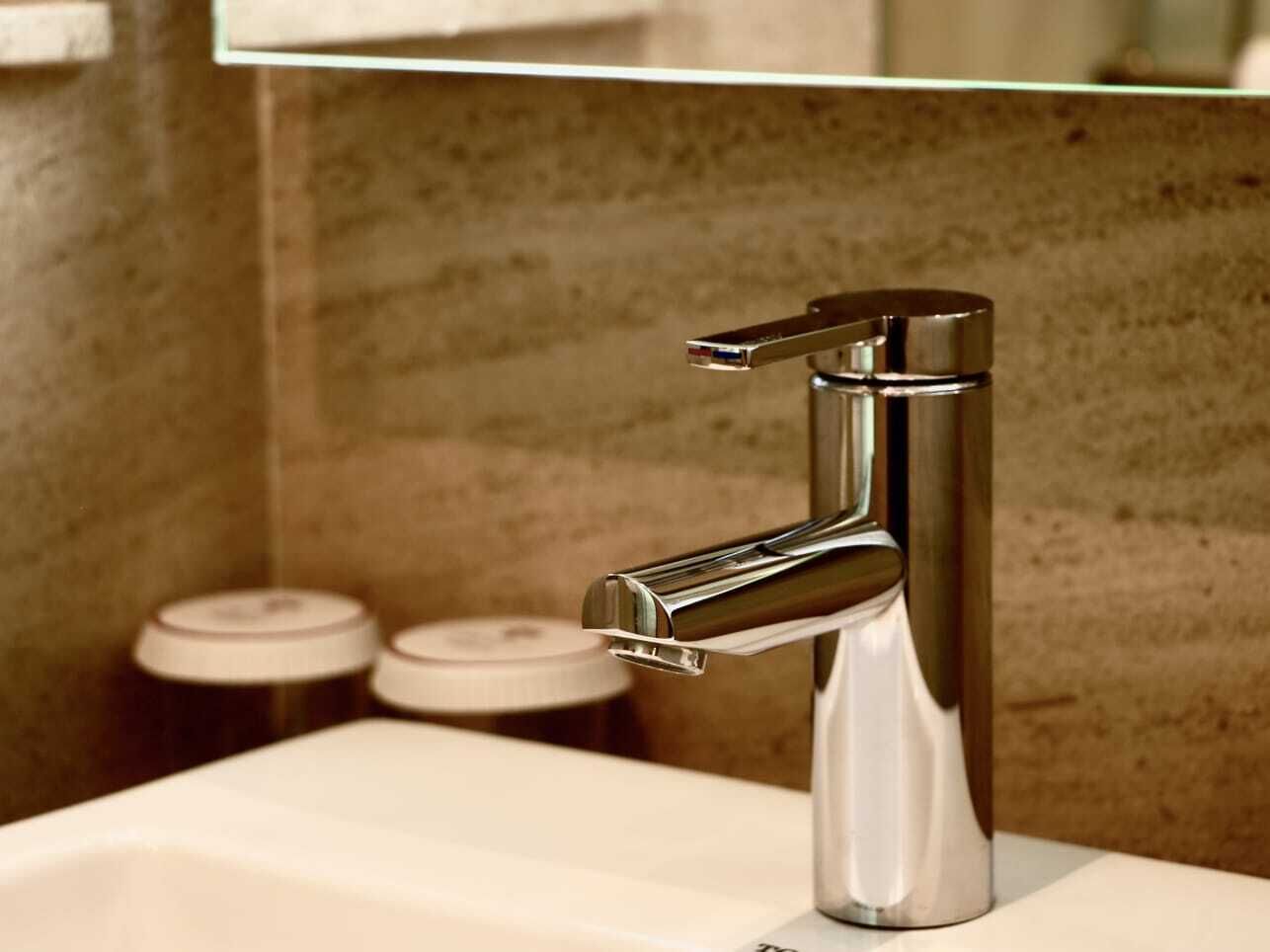 A modern bathroom with a chrome faucet, a white sink, and two soap dispensers on the wall.