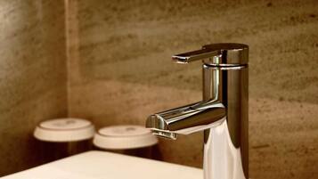 A modern bathroom with a chrome faucet, a white sink, and two soap dispensers on the wall.