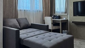 A modern hotel room with a sofa bed, a desk, a chair, a television, and large windows with curtains. - Kew Green Hotel Mongkok (Kowloon)