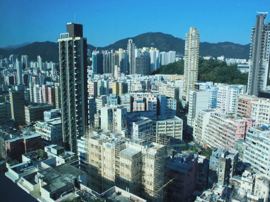 A dense urban area with high-rise buildings, some under construction with scaffolding, and a mountainous backdrop.