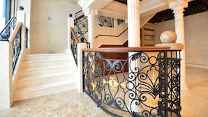 A grand staircase with marble steps and ornate black metal railings, leading to a landing with a wooden table and a decorative sphere. - Kew Green Hotel Mongkok (Kowloon)