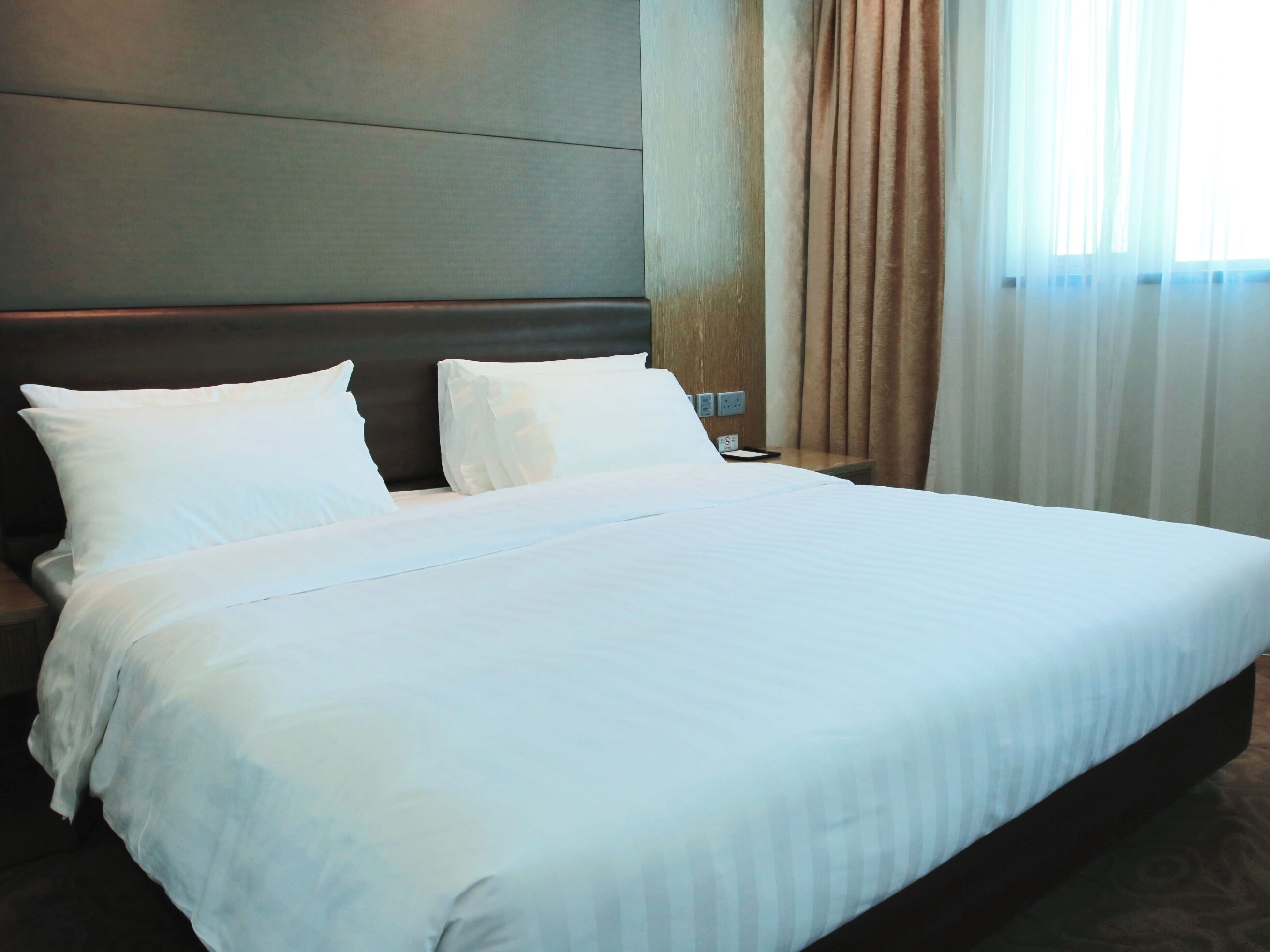 A neatly made bed with white linens in a hotel room.