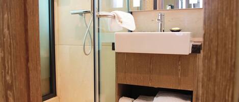 Un baño moderno con cabina de ducha acristalada, lavabo blanco y toallas ordenadas en un estante.