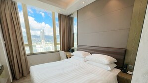 A hotel room with a large bed, a nightstand, a desk, and a view of a cityscape through the window. - Kew Green Hotel Mongkok (Kowloon)