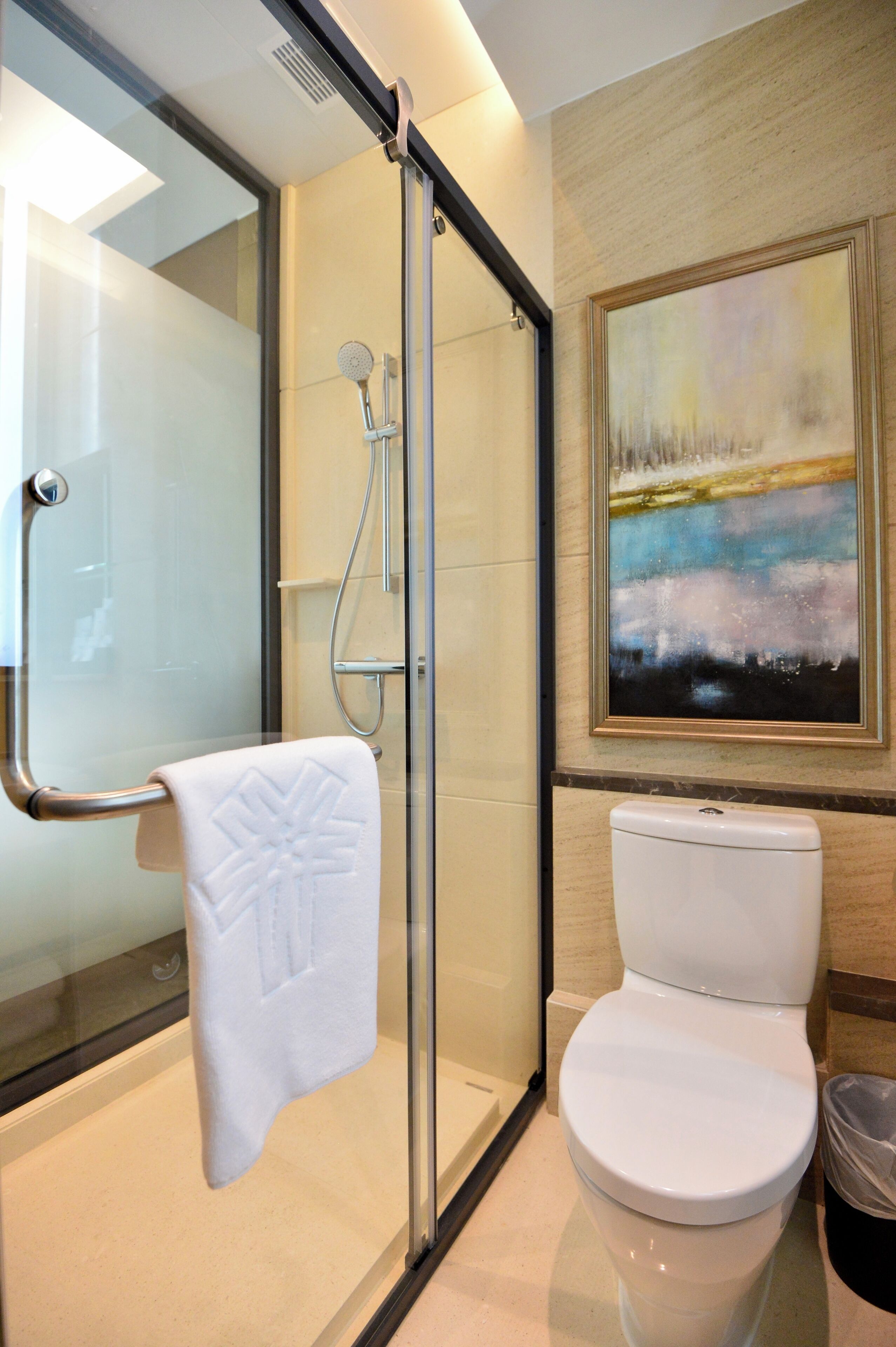 A modern bathroom with a glass-enclosed shower, a white toilet, and a large abstract painting on the wall.
