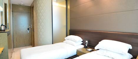 A hotel room with two beds, a wooden headboard, a nightstand with a lamp, and a bathroom with a shower and toilet.