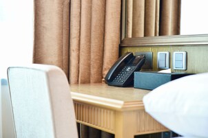 A hotel room with a wooden desk, a telephone, and a light switch.