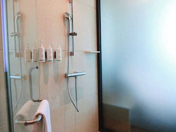 A bathroom with a glass shower enclosure, a towel rack, and several toiletries on the wall.