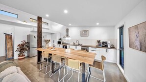 A modern kitchen with a wooden dining table, white cabinets, and a large window. - Escape to a unique house located in the world-renowned surf spot of Bells Beach! (Bells Beach)