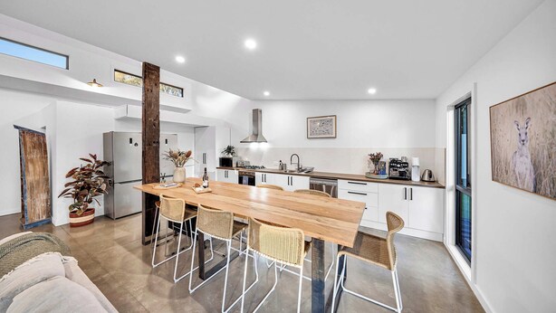 A modern kitchen with a wooden dining table, white cabinets, and a large window. - Escape to a unique house located in the world-renowned surf spot of Bells Beach! (Bells Beach)