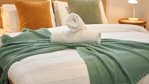 A neatly made bed with a green knitted blanket and a white towel, a wooden headboard, and a window with a view of trees. - Escape to a unique house located in the world-renowned surf spot of Bells Beach! (Bells Beach)