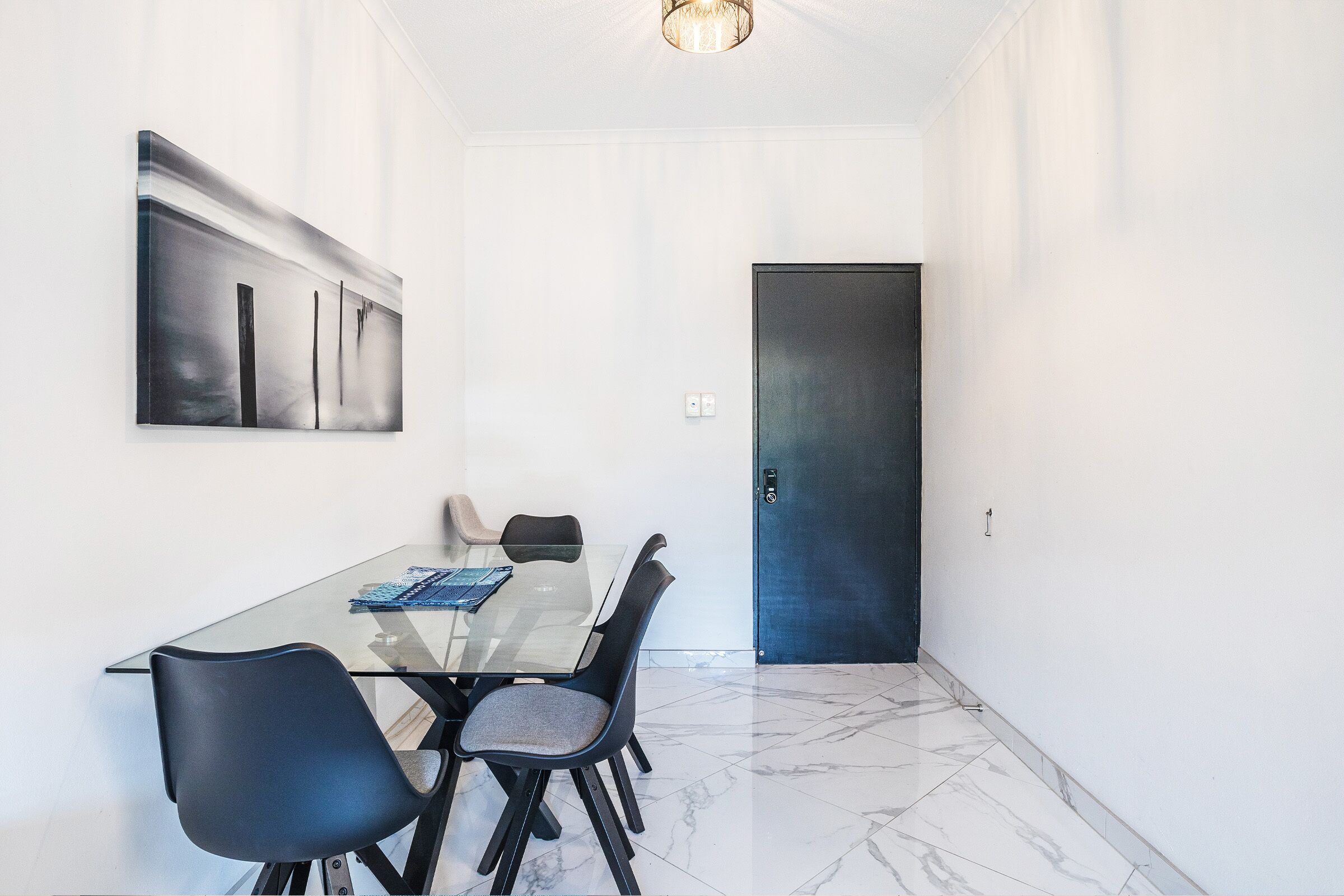 A modern dining area with a glass table, black chairs, and a minimalist painting on the wall.
