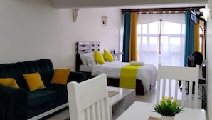 Een moderne, goed verlichte woonkamer met een bank, een eettafel en een bed met gele kussens.