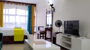 Een moderne hotelkamer met een bed, een bureau, een stoel, een televisie en een ventilator.
