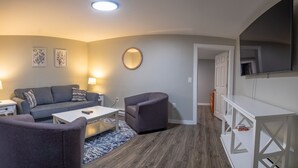 Un salon moderne avec un canapé gris, un petit fauteuil, une table basse blanche et un miroir rond accroché au mur.