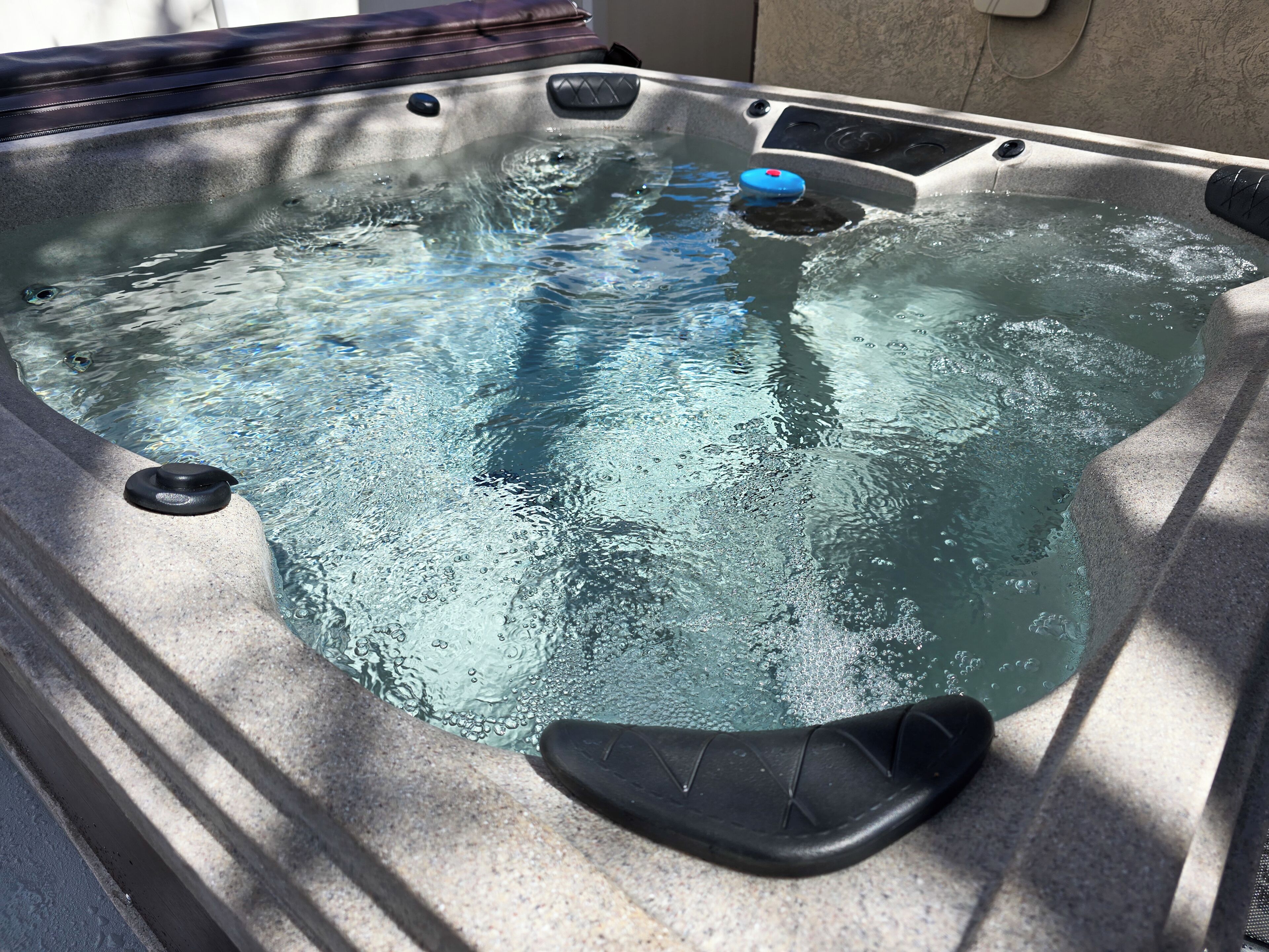 A hot tub with a control panel, a black seat, and a water pump.