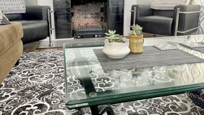 Ein Wohnzimmer mit Kamin, zwei schwarzen Ledersesseln, einem Glastisch und gemusterten Teppichen.