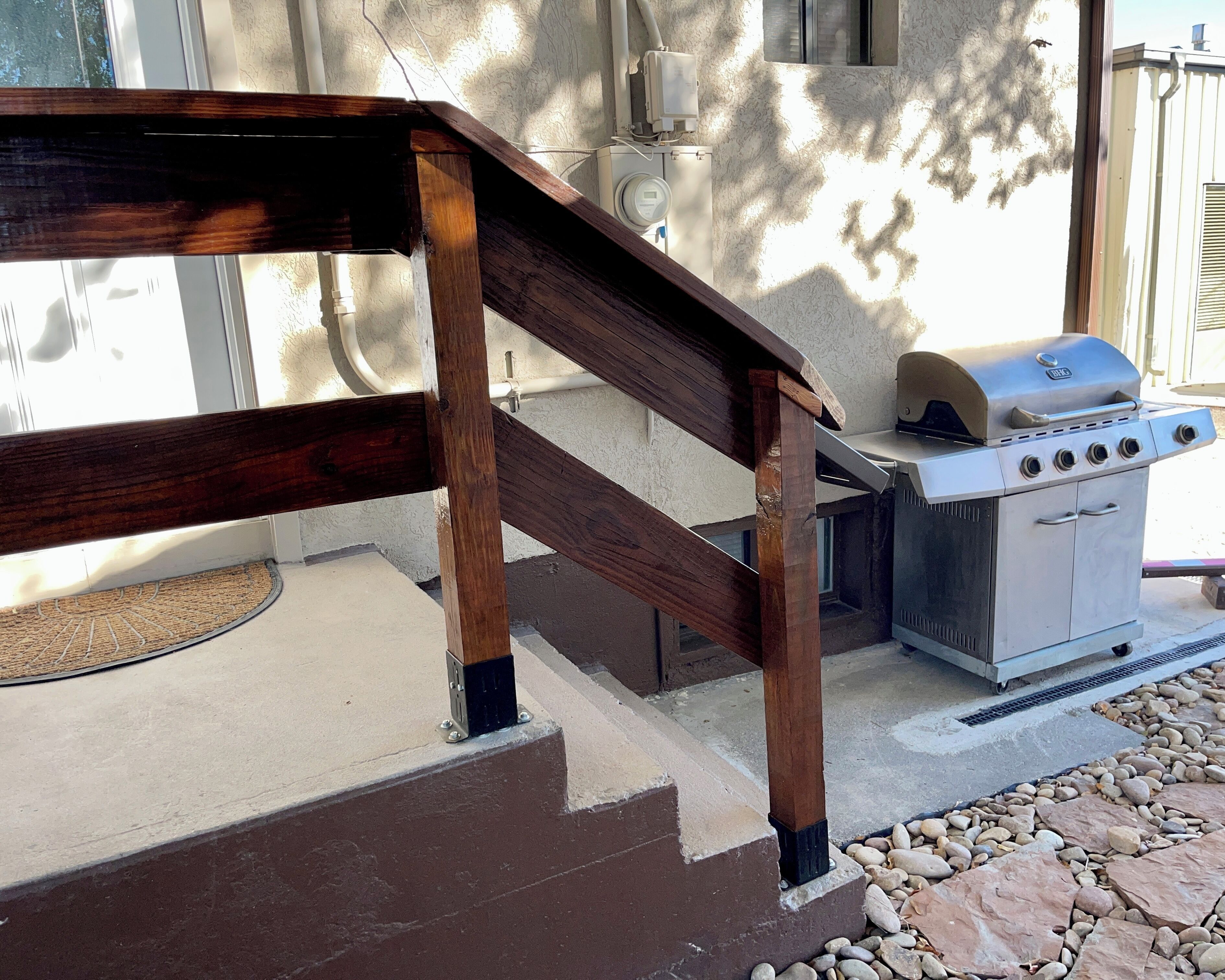 A wooden staircase leading to a patio area with a grill and outdoor seating.