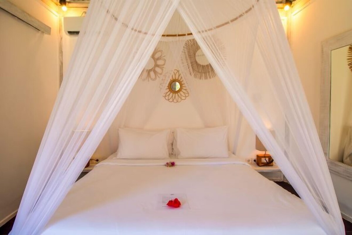 Una cama con dosel, ropa de cama blanca y una sola rosa roja sobre la cama.