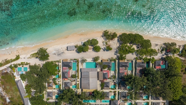 Vista aérea de un resort con varias construcciones, una playa y aguas turquesas cristalinas.