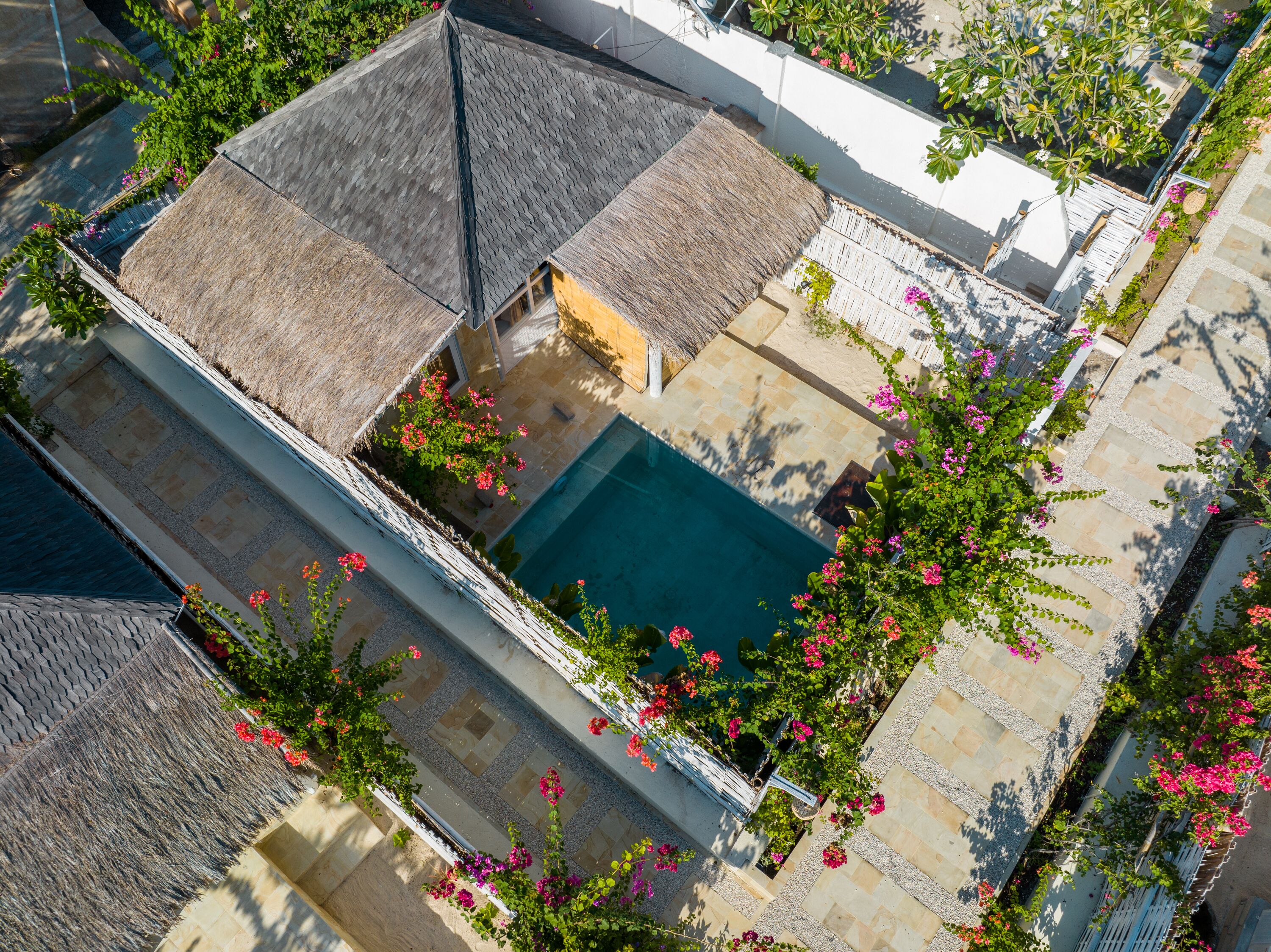 Una vista aerea di una zona residenziale con piscina circondata da vialetti in pietra e piante fiorite.