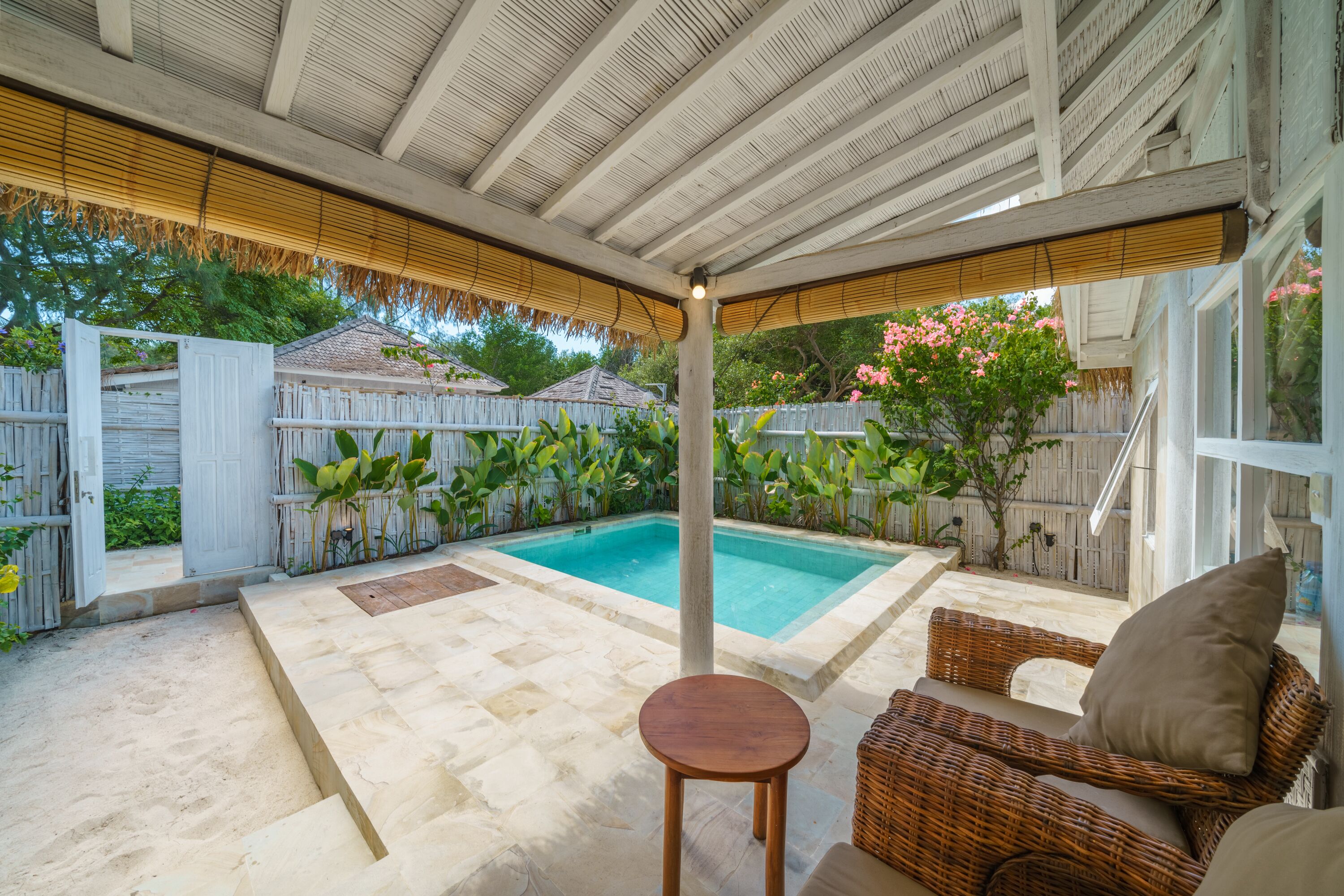 Un espace extérieur abrité comprenant une piscine, des meubles en osier et une clôture en bois.