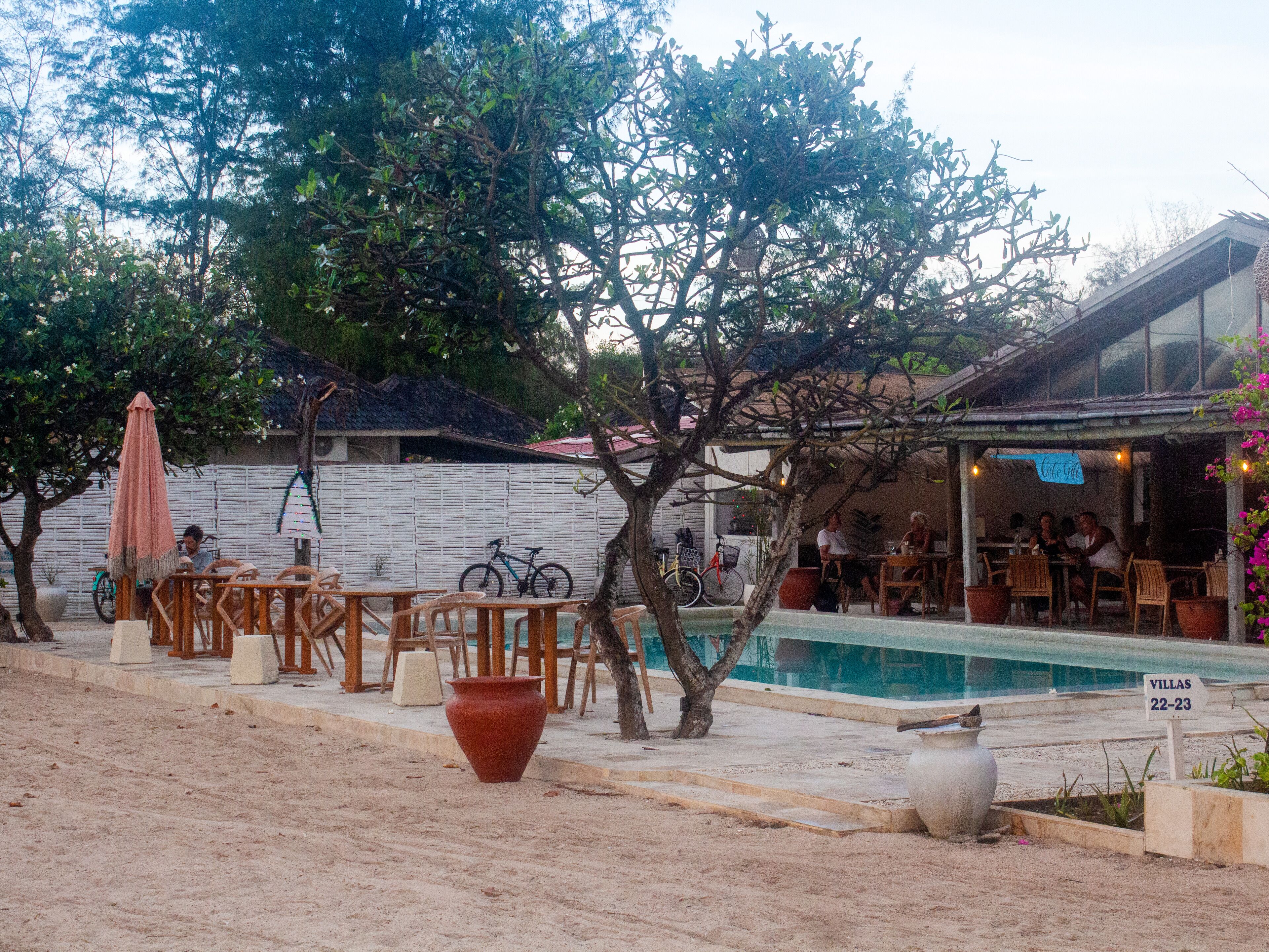 A poolside area with outdoor seating, a sign indicating 'Villas 22-23', and a bicycle parked near the pool.
