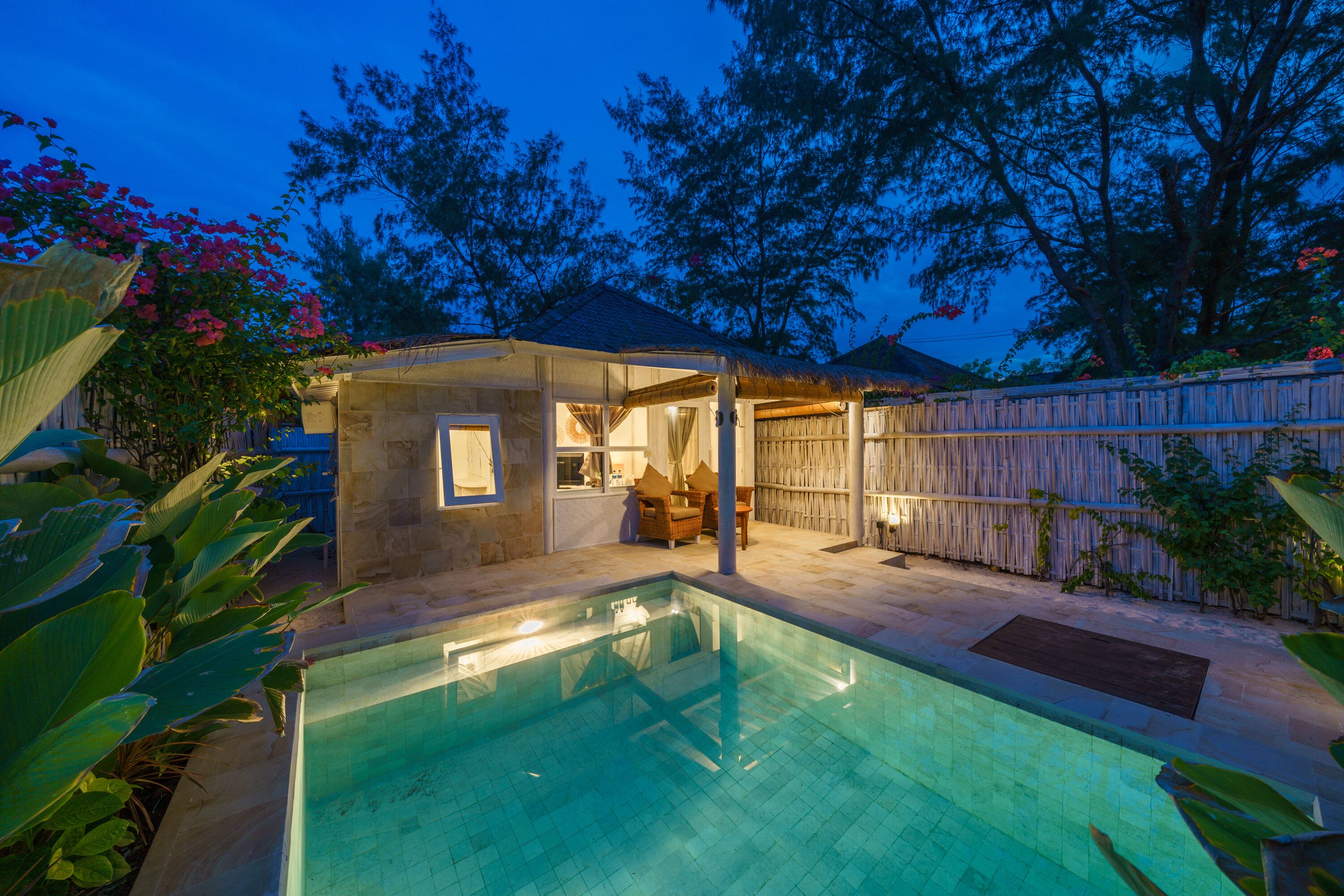 A backyard with a swimming pool, a small covered seating area, and a wooden fence.